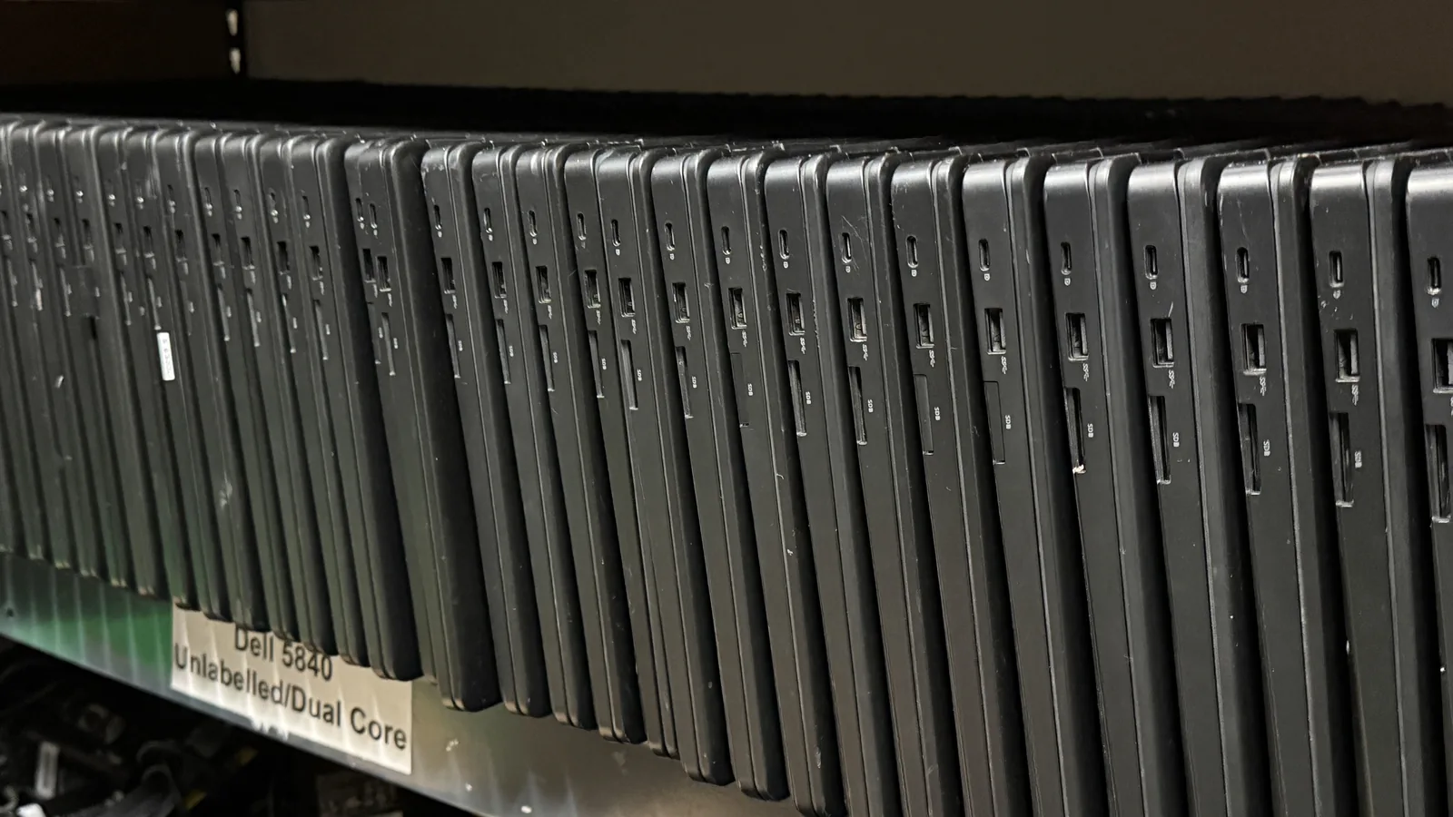 A shelf of Dell laptops stood on end in a row, seen along their edges