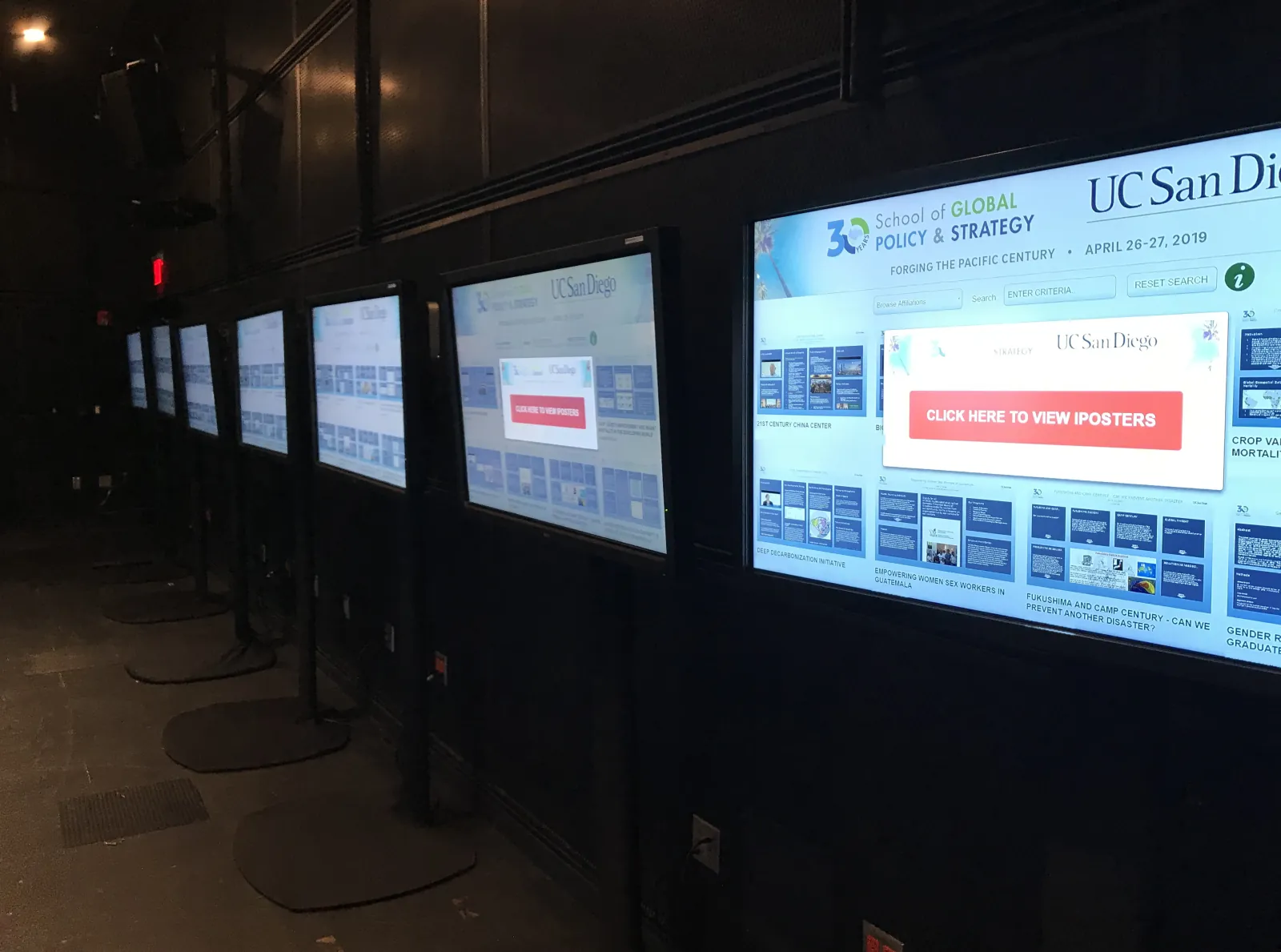 A row of large screens on floor stands showing digital posters at a university conference