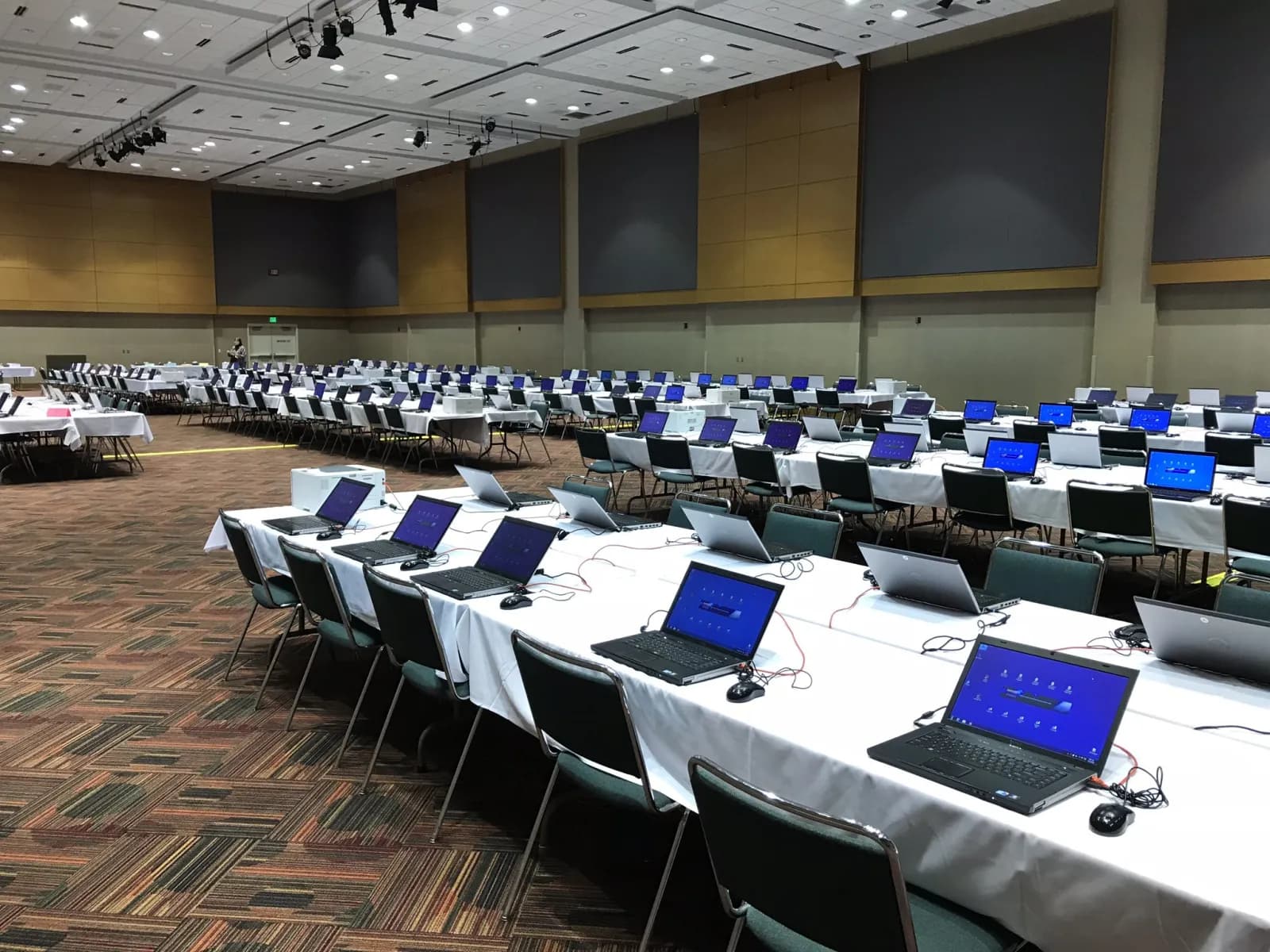 Long tables in a conference hall set with rows of laptops and mice, ready for attendees