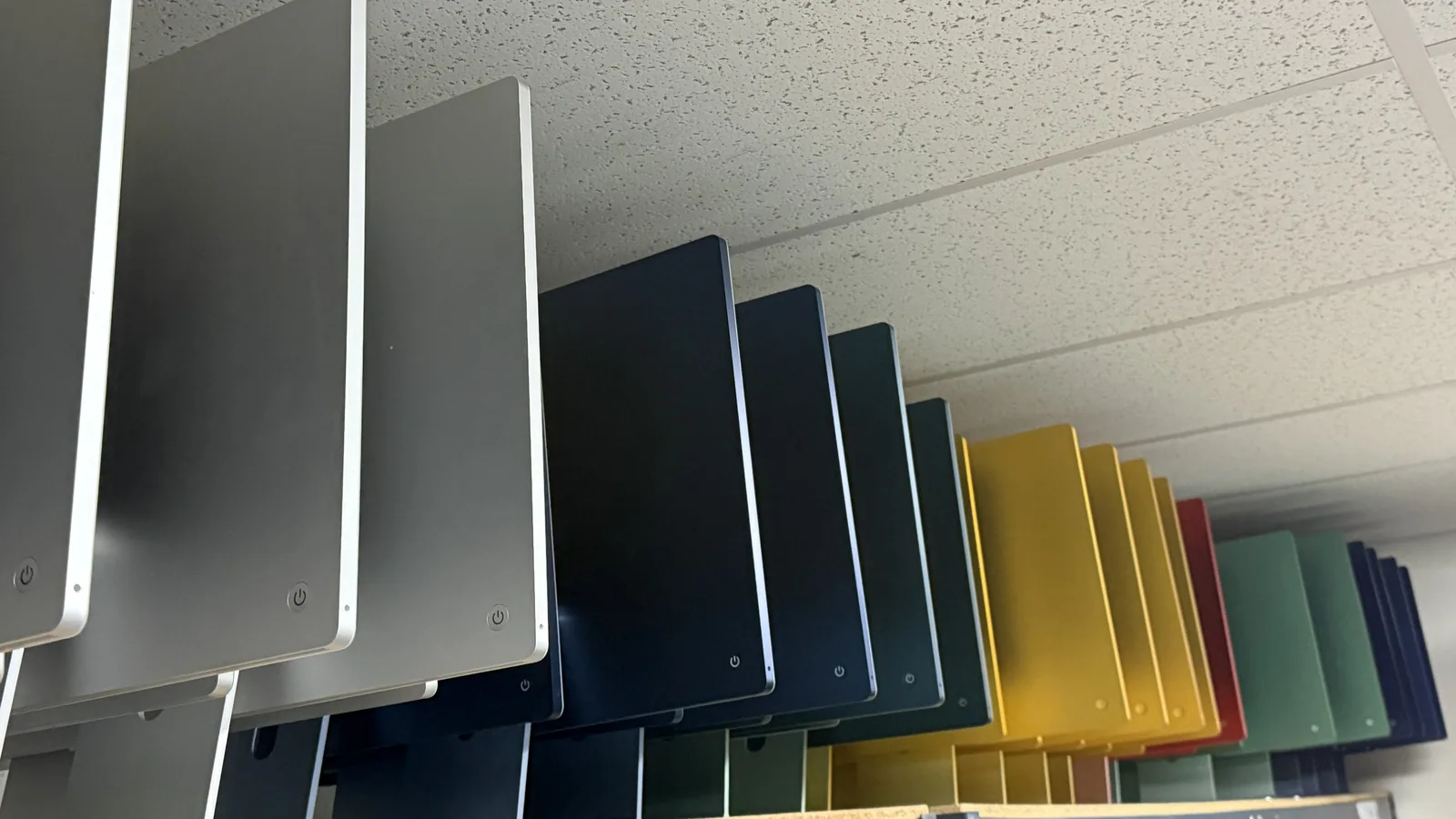 iMacs stacked on end on a warehouse shelf in silver, blue, yellow, red and green