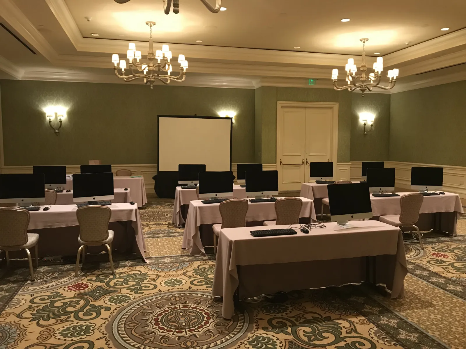 iMacs set out on draped tables in a hotel meeting room, with a projector screen at the front