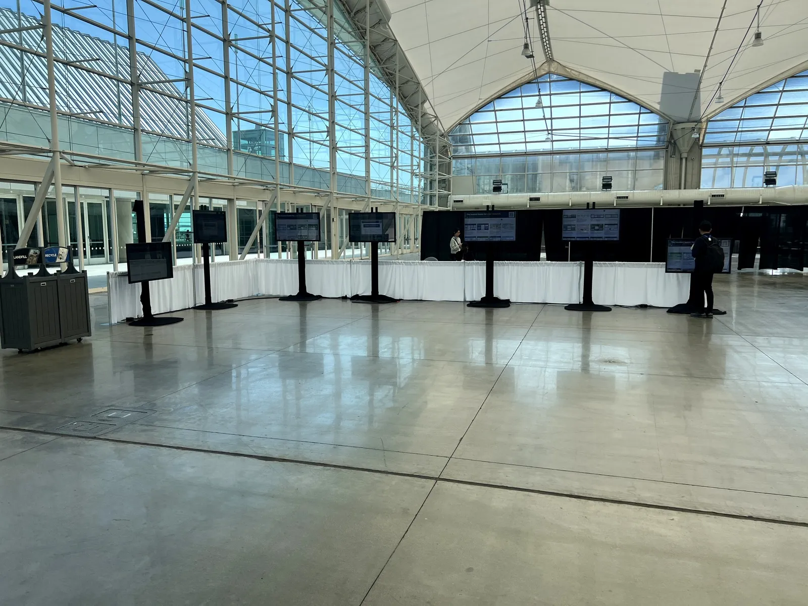 Displays on floor stands set out around a convention hall under a glass roof