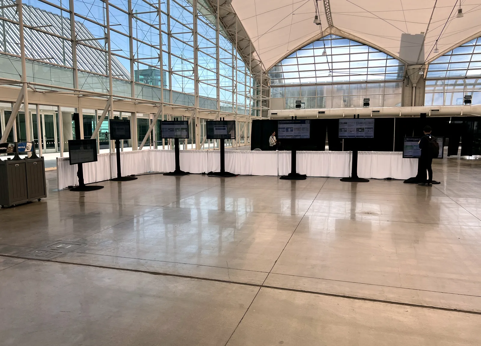 Displays on floor stands set out across a convention hall under a glass and fabric roof, before the doors open