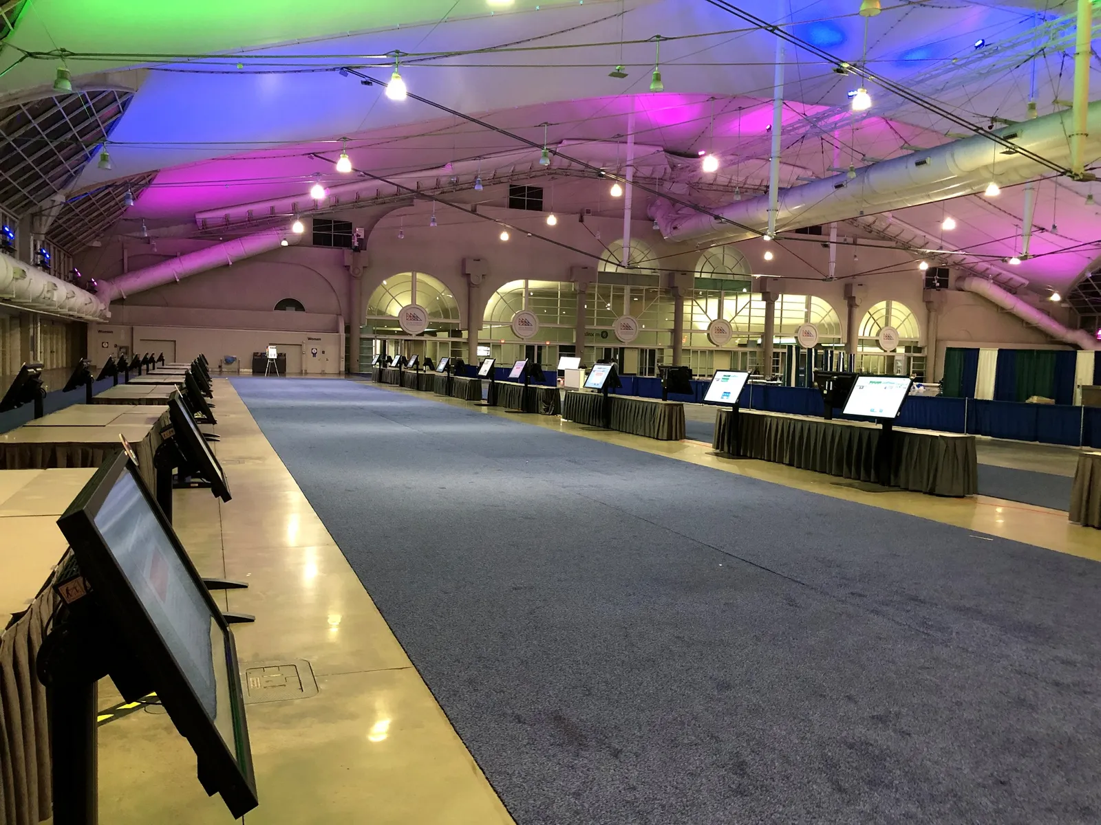 A long convention hall under colored lighting, with registration tables and screens along a blue carpet