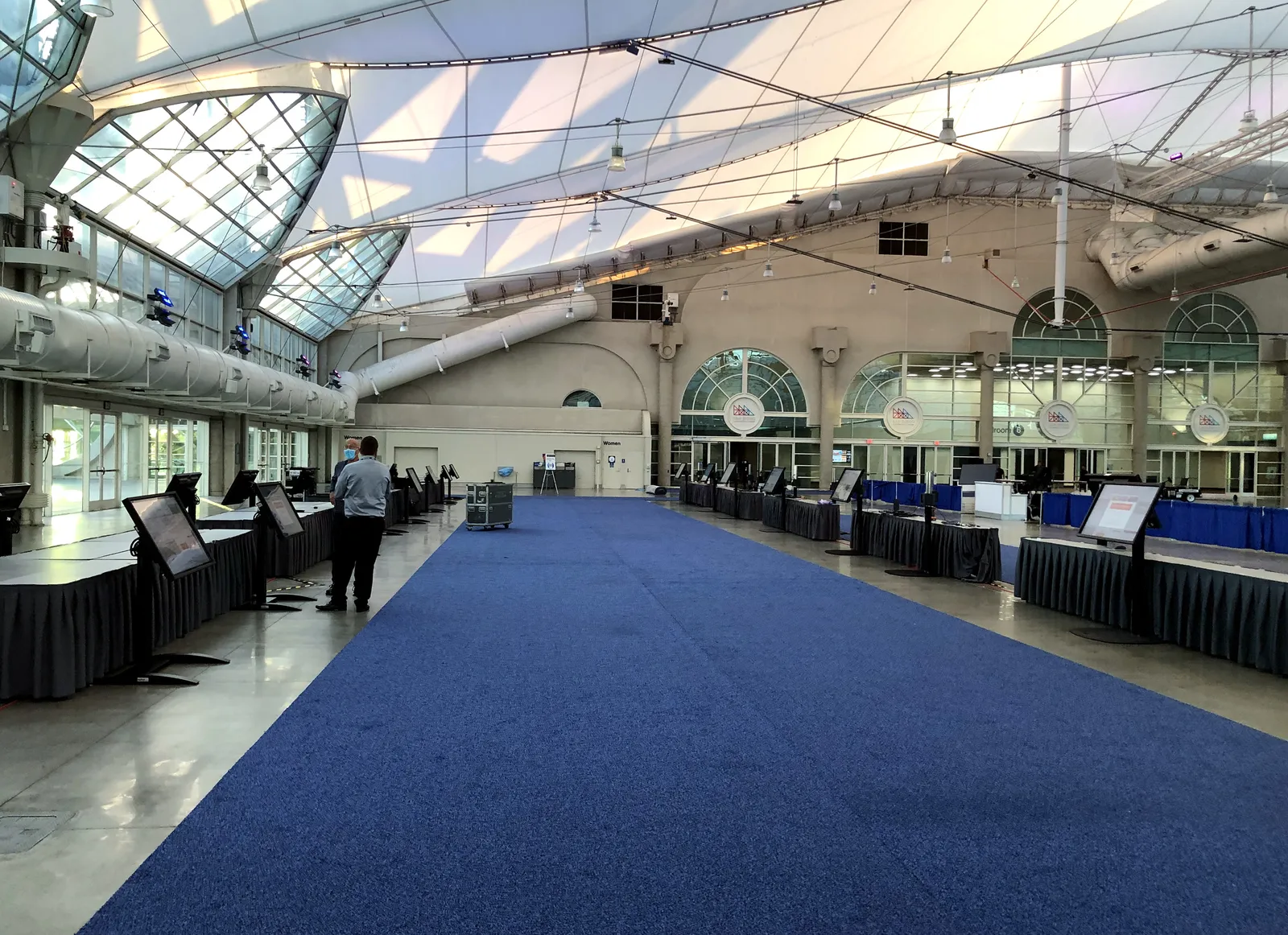 A long convention hall set with draped tables and screens, before the doors open