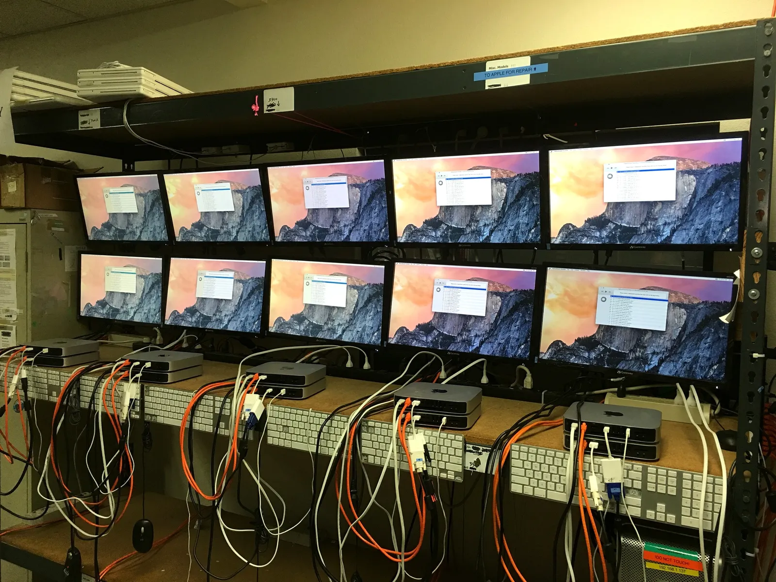 Two rows of monitors on warehouse shelves, cabled up and switched on while they are tested