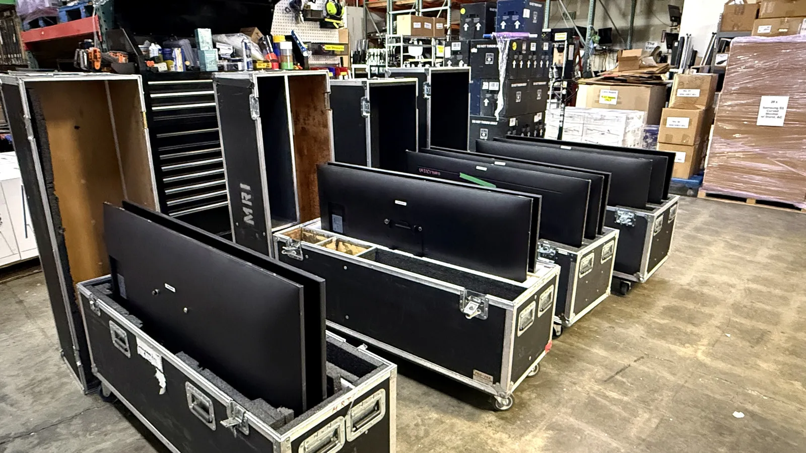 Computer monitors packed upright in open flight cases on the warehouse floor