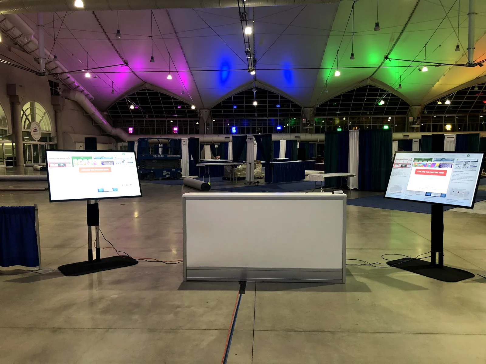 Two touchscreen check-in kiosks on floor stands beside a counter in a convention hall